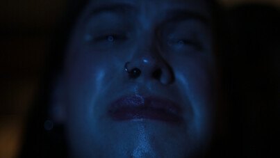 Still from Jamie Crewe's Ashley: a face lit in blue